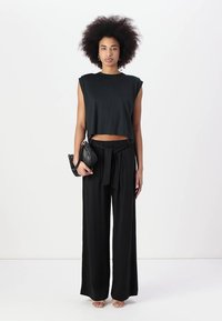 Top negro recortado sin mangas de corte relajado, combinado con pantalones anchos de tiro alto en negro, atados en la cintura. Sencilla bolsa negra.