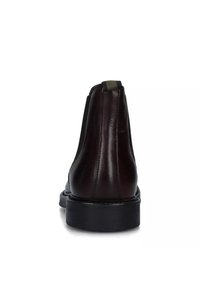 Stivaletto in pelle marrone scuro con suola nera, cuciture visibili e una linguetta in tessuto sul retro, visto da dietro.