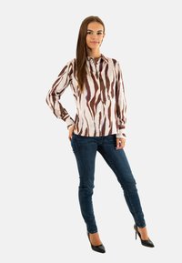 Camicia a maniche lunghe, con bottoni, di base crema chiaro e ampie strisce marroni e viola. Abbinata a jeans skinny blu e tacchi neri.