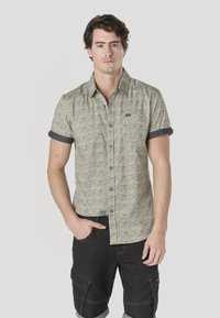 Short-sleeve button-up shirt in a textured green and gray pattern, with a dark blue roll-up accent at the sleeves and subtle logo detailing.