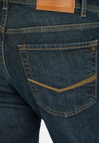 Donkerdenim jeans met een driehoekig zakontwerp. Voorzien van een bruine leren logo patch en contrasterende goudgele stiksels.