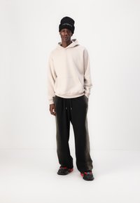 Sweatshirt i lys beige med hætte og frontlomme, parret med sorte tapered joggers. Textureret sort beanie, kraftige sorte sko med røde accenter.