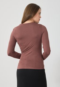 Garais piedurknes tops maigā mauve krāsā, izgatavots no mīksta, elastīga auduma. Iezīmē apaļu kakla izgriezumu un pieguļošu siluetu, viegli kombinējams ar dažādām apakšdaļām.