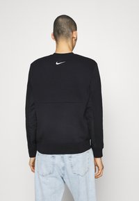 Svart sweatshirt med rund hals, med en slät textur och ribbat ärmslut. En vit Nike-logotyp är placerad på den övre delen av ryggen.