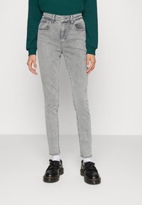 Jeans de tiro alto en gris claro con un diseño ajustado, cinco bolsillos y un ligero desvanecimiento. Combinados con zapatos negros y calcetines blancos.