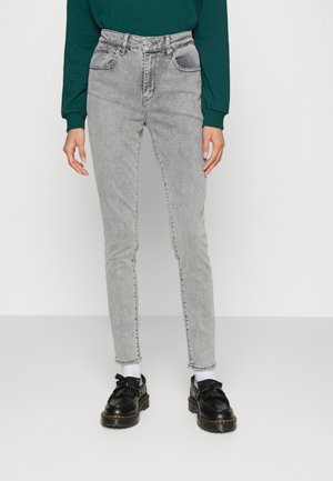 Jeans de tiro alto en gris claro con un diseño ajustado, cinco bolsillos y un ligero desvanecimiento. Combinados con zapatos negros y calcetines blancos.