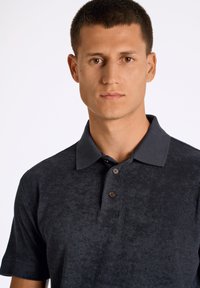 Tummanharmaa polo-paita pehmeällä tekstuurilla, klassisella kauluksella, kolmella napilla ja lyhyillä hihoilla. Sisältää ruskeat napit.
