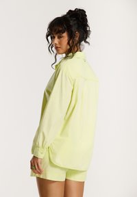 Limoengroene, oversized blouse met lange mouwen, een afgeronde zoom en bijpassende shorts. Gladde textuur met een subtiele glans.
