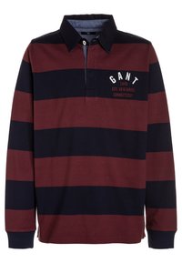 Langärmliges Rugby-Shirt mit breiten horizontalen Streifen in Marineblau und Kastanienbraun, schwarzem Kragen und weißem Text "GANT 1949 EST. NEW HAVEN CONNECTICUT" auf der Brust.