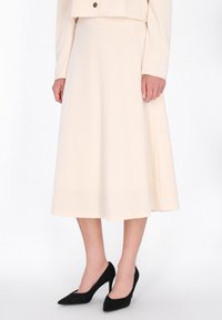 Vaaleanbeige midi-hame, joka on valmistettu sileästä kankaasta ja jossa on virtaava siluetti. Yhdistetty mustiin kärjellisiin korkokenkiin kontrastiksi.