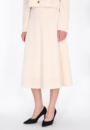 Licht beige midi-rok gemaakt van een soepele stof, met een vloeiende silhouet. Gedragen met zwarte puntige hakken voor contrast.