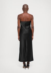 Vestido negro de satén sin tirantes con un corsé ajustado y una falda fluida, con una costura en la parte trasera, acompañado de zapatos de tacón alto negros.