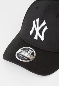 Gorro negro con visera curvada, que presenta un logotipo bordado en blanco de "NY". Incluye una etiqueta plateada con las inscripciones "9FIFTY" y "STRETCH-SNAP".