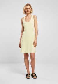 Vestido sin mangas de color amarillo claro con escote redondo, confeccionado en un material suave. Presenta un ajuste relajado y cae por encima de las rodillas.