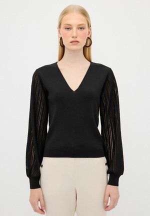 Schwarzer Strickpullover mit V-Ausschnitt und langen, transparenten Ärmeln, die vertikale Streifen aufweisen. Gerippte Bündchen und Saum mit taillierter Passform.