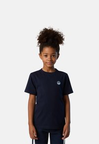Camiseta de algodón navy de manga corta, con cuello redondo, logo bordado en el pecho. Textura suave, ajuste casual. Llevada con pantalones a juego.