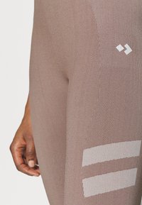 Burgundzkie legginsy sportowe z teksturowanej tkaniny, z odblaskowymi białymi paskami i małym logo w pobliżu pasa.