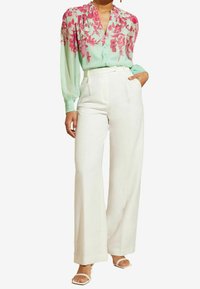 Blusa de manga larga en menta clara con un patrón floral rosa, combinada con pantalones blancos de pierna ancha y talle alto, y sandalias blancas de tiras.