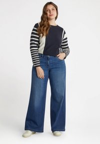 Pull à rayures bleu marine et crème à manches longues associé à un jean bleu à jambes larges. Le jean présente une légère décoloration et un design classique à cinq poches.
