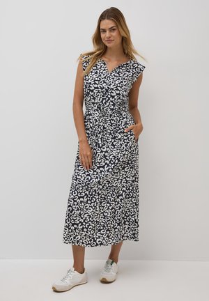Abito maxi in blu navy con stampa leopardata astratta bianca, maniche corte a cappuccio, scollo a V e gonna a livelli. Abbinato a scarpe sportive bianche.