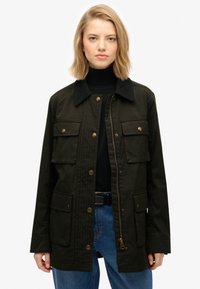 Chaqueta verde oscuro con cuello de pana, cremallera frontal y botones a presión. Cuenta con cuatro bolsillos frontales y un patrón acolchado en el pecho.