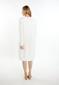 Cardigan lungo bianco realizzato in materiale soffice con taglio dritto. Il design presenta maniche lunghe e un orlo che arriva a metà polpaccio.