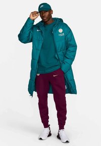 Jachetă pufosă teal cu glugă, pantaloni jogger vișinii și adidași albi. Branding Nike pe jachetă și pe căciulă. Prezintă o textură netedă și o croială casual.