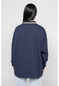 Suéter oversized azul marino con cuello acanalado y acentos texturizados. Presenta hombros caídos y un ajuste relajado.