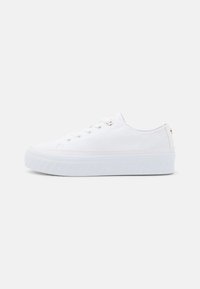 Baskets en toile blanche avec une semelle épaisse blanche, un design à lacets et des œillets dorés. Texture lisse et style minimaliste.