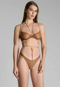 Bikini marron avec un haut triangulaire transparent à fines bretelles et un bas taille haute assorti, accentué par des détails en métal doré.