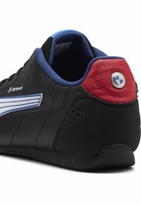 Schwarzer Sportschuh mit blauen Akzenten und roter Ferse. Verfügt über weiße Streifen und ein rundes blaues Emblem an der Ferse. Geriffelte Gummisohle.