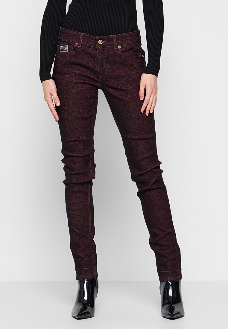 Burgundzkie wąskie dżinsy o gładkiej fakturze, z zapięciem na guzik i przednimi kieszeniami, zestawione z błyszczącymi czarnymi botkami za kostkę.