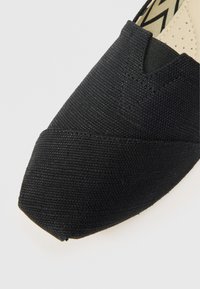 Czarny wsuwany but wykonany z teksturowanej tkaniny, z zaostrzonym noskiem i minimalistycznymi przeszyciami, prezentujący elegancki, nowoczesny design.