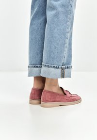 Mocassini in suede rosa con suola piatta color tan, mostrati con jeans azzurri arrotolati, che rivelano un risvolto e dettagli di cucitura visibili.
