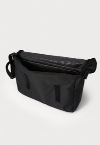 Sac messager noir en tissu durable, doté d'une fermeture Velcro, d'un intérieur spacieux, d'une sangle réglable et d'un motif de logo discret à l'intérieur.