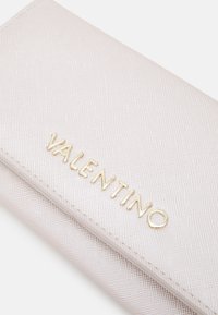 Pink textured wallet made of synthetic material. Features gold "Valentino" logo in bold lettering on the front. Zippered closure visible.