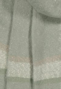 Helle grüne Schal mit weicher Textur, der horizontale Streifen in Beige und dunklerem Grün aufweist. Der Stoff wirkt flauschig und warm.