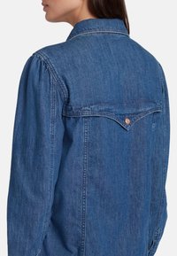 Denim overhemd in middelblauw met lange mouwen, een button-down kraag en een gestikte achterste yoke detail. Zachte textuur, klassieke pasvorm.