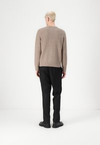 Light brown knit sweater with a textured pattern, round neckline, and ribbed cuffs. Black pants with a relaxed fit and visible rear pockets.