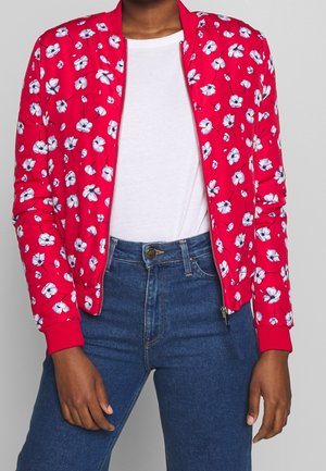 Rød bomberjakke med blomsterdesign i blå og hvid, ribbede manchetter og krave, lynlåslukning, parret med en hvid top og blå jeans.