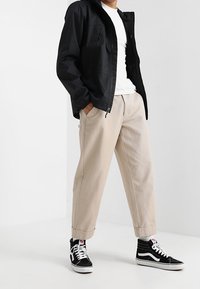 Černá lehká bunda s kapucí, bílé tričko, béžové kalhoty volného střihu a černé tenisky s vysokým svrškem a bílými detaily.