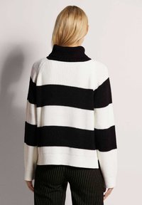 Zwart-wit gestreepte trui met een geribbelde textuur, coltrui en verlaagde schouders, gestyled met smal gestreepte broek.