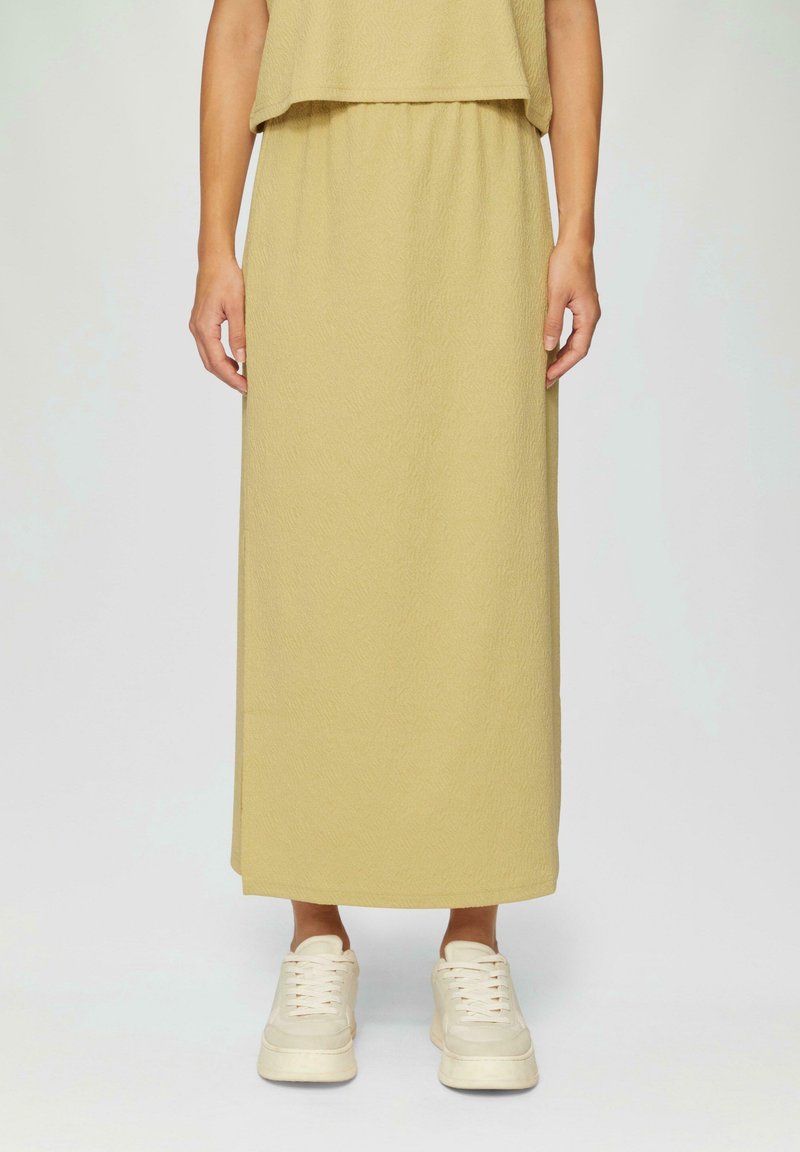 Robe longue, légère et texturée de couleur jaune pâle. Dotée d'une taille élastique et d'une coupe ample, portée avec des baskets blanches.