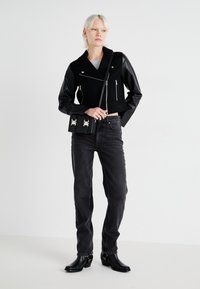 Svart cropped jakke med ullkropp og lær-ermer, kombinert med mørk denimbukser og ankelstøvler. Holder en liten svart veske med sølvdetaljer.