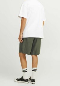 En vit t-shirt, olivgröna shorts, svarta sneakers och vita strumpor med svarta ränder. Avslappnad outfit sedd bakifrån.