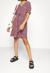 Květinové šaty v černé barvě s růžovými květinami, krátké plandavé rukávy, výstřih do V a sukni s volány. V kombinaci s černými platformovými sandály a bílou taškou.