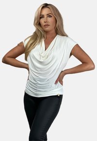 Biała bluzka z krótkimi rękawami, wykonana z miękkiego, gładkiego materiału, z marszczeniami w talii i subtelnym złotym akcentem na czarnych, slim fit spodniach.