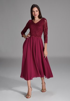 Abito bordeaux con top in pizzo caratterizzato da scollatura a V e maniche a 3/4. Gonna in chiffon fluida con orlo al ginocchio, completata da sandali dorati.
