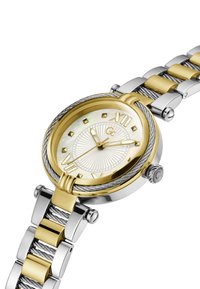 Kulaté hodinky se zlatým rámečkem a ciferníkem z perleti. Římské číslice, stříbrný náramek z jemné sítě se zlatými akcenty. Nerezová ocel.