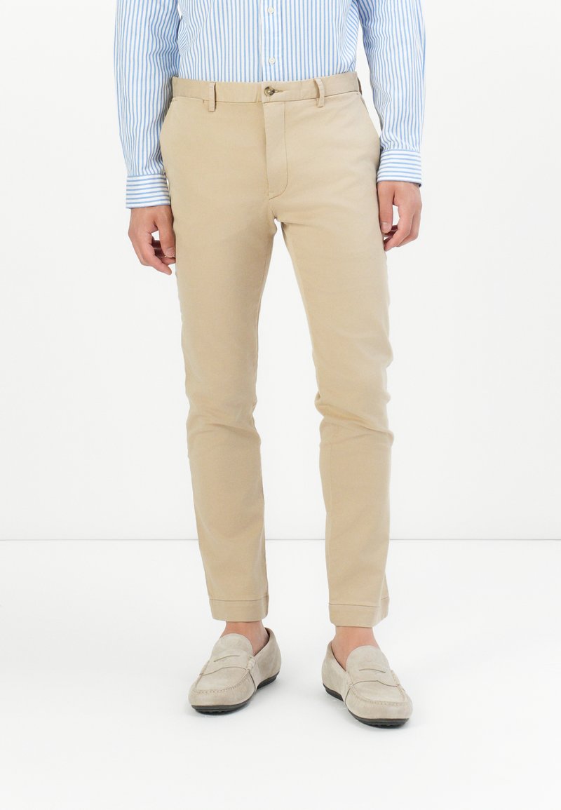 Beżowe bawełniane spodnie z wąskim krojem, prostymi nogawkami i płaskim przodem. Posiadają zapięcie na guzik oraz boczne kieszenie.
